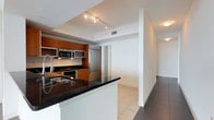 This well-appointed single-floor residence features three bedrooms and two and a half bathrooms, thoughtfully designed to maximize comfort and functionality. The heart of the home is a sleek, open-concept kitchen that seamlessly connects to the living areas, creating an ideal environment for both entertaining and everyday living. The kitchen is outfitted with rich warm-toned wood cabinetry, dark granite countertops, and a full suite of stainless steel appliances, including a built-in microwave, gas range, and refrigerator. A kitchen island with an integrated sink adds additional prep space and serves as a natural gathering point. Track lighting above the kitchen illuminates the space with a clean, modern aesthetic. Large format tile flooring flows throughout the common areas, providing a cohesive and polished look, while the crisp white walls and ceilings enhance the sense of openness and brightness. A hallway connects the main living spaces to the private bedroom quarters, maintaining a clear and logical flow throughout the floor plan. The overall ambiance is contemporary and refined, with a neutral palette and quality materials that lend the space a timeless, move-in-ready appeal.
