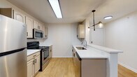 This single-floor residence offers a thoughtfully designed layout with a clean, updated aesthetic throughout. The kitchen serves as a central highlight, featuring cream-toned cabinetry with modern black hardware, stainless steel appliances including a full-size refrigerator, electric range, and built-in microwave. A white quartz peninsula with an undermount sink provides additional prep space and casual seating potential, while a striking multi-bulb pendant light fixture adds a contemporary touch overhead. Light wood-look flooring runs throughout the kitchen and main living areas, contributing to a bright, cohesive feel.

The bedrooms are finished with neutral carpet and ceiling fans, creating comfortable, well-ventilated spaces. Each bedroom includes closet storage, with one room featuring French doors that open to the exterior, introducing natural light and outdoor access. A louvered closet near the entry provides additional storage convenience.

The bathroom is finished with wood-look flooring and features a tiled tub-and-shower combination with a classic white tile surround accented by a black tile border. A framed mirror, vanity with cabinet storage, and a well-lit fixture complete the space. Overall, the unit presents a clean, functional, and move-in-ready environment.