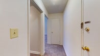 This single-floor unit presents a clean, functional layout with a neutral color palette throughout. The living area is generously sized, finished with wall-to-wall carpet and bright white walls that create an open, airy feel. A wide bank of windows along one wall floods the space with natural light while offering views of the surrounding outdoor landscape. Baseboard heating units are present throughout, providing consistent warmth.

The kitchen is efficiently designed, featuring dark speckled countertops, a stainless steel sink, white cabinetry both above and below the counter, and a black gas range, offering practical workspace for everyday cooking. The layout connects smoothly to the rest of the unit.

The bedroom areas are carpeted and well-proportioned, each with its own natural light source. One bedroom includes a built-in sliding-door closet with shelving, offering organized storage. A carpeted hallway connects the rooms, with additional closet space accessible along the corridor.

The bathroom is finished in white ceramic tile surrounding a full soaking tub with overhead shower. A window provides natural ventilation, and a vanity with cabinet storage completes the space. Overall, the unit offers a straightforward, comfortable interior well-suited for everyday living.