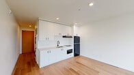 Located at 1341 N Killingsworth St in Portland, Oregon, this efficiently designed single-floor studio offers a clean, modern aesthetic throughout. Light hardwood flooring runs continuously across the entire space, complementing the crisp white walls and lending a bright, cohesive feel.

The open-plan living and kitchen area makes excellent use of the available footprint. The kitchen is outfitted with white flat-front cabinetry extending to the ceiling for generous storage, a light-toned countertop with an undermount sink, a black refrigerator, and recessed lighting overhead. A subway tile backsplash adds a subtle design detail. A stacked washer and dryer unit is neatly integrated into a dedicated alcove, keeping laundry facilities conveniently in-unit without encroaching on living space.

The living area is anchored by a door flanked by tall windows that invite abundant natural light and provide views of the surrounding Portland neighborhood. A second window along the side wall further enhances the airy atmosphere.

The bathroom maintains the home's clean, minimalist design language, featuring a white vanity with an undermount sink, black hardware accents, and the same hardwood-style flooring found throughout the rest of the unit. The overall ambiance of this space is modern, functional, and well-appointed, making it a practical and stylish option in North Portland.