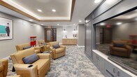 Located at 6822 Shannon Pky in Union City, GA, this thoughtfully designed screening and entertainment lounge offers a refined yet inviting atmosphere ideal for communal gatherings. The single-floor space is anchored by a striking tray ceiling with warm wood trim accents and recessed lighting, creating a layered, intimate ambiance reminiscent of a private cinema.

The living area is furnished with plush tan leather armchairs arranged in a theater-style configuration, each accompanied by sleek round side tables with built-in cup holders, ensuring comfort during extended viewing sessions. A large built-in media wall finished in a sophisticated slate-gray cabinetry anchors one side of the room, while a window on the opposite wall allows natural light to filter in.

A dedicated wet bar station lines one wall, featuring warm wood cabinetry, a white subway tile backsplash, a matte black faucet, and a clean white countertop — perfect for refreshments. Classic movie posters adorn the walls, adding a cinematic character to the space, while a vintage-style red popcorn machine serves as both a functional and decorative focal point.

The patterned carpet in soft blue and gray tones ties the design together, complementing the neutral gray walls and overall contemporary aesthetic of this well-appointed entertainment space.