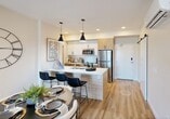 Located at 150 Edgemont Road NW in Edmonton, Alberta, this well-appointed 2-bedroom, 2-bathroom unit offers a thoughtfully designed open-concept layout. Light oak-toned luxury vinyl plank flooring flows throughout, complementing the bright, neutral palette that gives the space an airy, contemporary feel.

The kitchen serves as a central hub, featuring a large island with a white quartz countertop, a double undermount sink, and bar seating for casual dining. Warm wood cabinetry is paired with stainless steel appliances, while bold black pendant lights add a modern accent overhead. The kitchen opens seamlessly into the dining and living areas, where a sliding glass door floods the space with natural light and provides access to an outdoor view.

The primary bedroom offers a comfortable retreat with a window framing pleasant neighbourhood views. Both bathrooms are finished with wood-toned vanities, white quartz countertops, and clean tile work. A dedicated den provides a quiet, functional space suitable for a home office. Additional practicalities include an in-unit laundry area, a pantry, and a closet for generous storage. The second bedroom is well-proportioned with direct access to the main living area, rounding out a practical and modern floor plan.