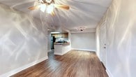 This single-story residence is designed with an open-concept layout that connects the living area and kitchen seamlessly. The living space features warm wood-look flooring that extends throughout, neutral-toned walls, and a textured ceiling with a ceiling fan, creating a comfortable and inviting atmosphere. Track lighting provides additional illumination, complementing the overall brightness of the space. A closet with louvered bifold doors offers convenient storage within the main living area.

The kitchen is a standout feature, highlighted by a skylight that floods the space with natural light. It is outfitted with granite countertops in warm earth tones, light wood cabinetry, and stainless steel appliances including a refrigerator and electric range. A double-basin sink is integrated into the peninsula, which also serves as a natural divider between the kitchen and living area, ideal for casual dining or meal preparation. The kitchen's layout is efficient, with ample counter space and cabinetry providing generous storage. The combination of the skylight, granite surfaces, and modern appliances gives the kitchen a polished, functional character that anchors the overall design of the space.