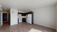 This single-floor unit offers a clean, contemporary design with wood-tone laminate flooring that flows seamlessly throughout every room, creating a cohesive and polished look. The open-concept layout connects the kitchen and living area, maximizing the sense of space and encouraging an easy, functional flow between the two zones.

The kitchen is a standout feature, fitted with rich dark espresso cabinetry accented by sleek bar-pull hardware, providing a striking contrast against the light-colored countertops and crisp white appliances. A full suite of appliances is included — refrigerator, range, microwave, and dishwasher — all set within an efficient L-shaped layout that maximizes counter and storage space.

The bedroom is a quiet, well-proportioned retreat featuring neutral walls, warm wood-tone flooring, and a built-in closet with a sliding dark-panel door that adds a modern architectural touch. Natural light filters in, further enhancing the room's airy feel.

The bathroom is thoughtfully designed to match the unit's overall aesthetic, featuring the same dark espresso cabinetry with a white countertop vanity, a large mirror, and wood-tone flooring. A full tub-shower combination and standard fixtures complete the space with clean, practical functionality. Overall, this unit presents a well-balanced combination of modern style and everyday comfort.