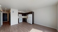 This single-floor unit offers a clean, contemporary design with wood-tone laminate flooring that flows seamlessly throughout every room, creating a cohesive and polished look. The open-concept layout connects the kitchen and living area, maximizing the sense of space and encouraging an easy, functional flow between the two zones.

The kitchen is a standout feature, fitted with rich dark espresso cabinetry accented by sleek bar-pull hardware, providing a striking contrast against the light-colored countertops and crisp white appliances. A full suite of appliances is included — refrigerator, range, microwave, and dishwasher — all set within an efficient L-shaped layout that maximizes counter and storage space.

The bedroom is a quiet, well-proportioned retreat featuring neutral walls, warm wood-tone flooring, and a built-in closet with a sliding dark-panel door that adds a modern architectural touch. Natural light filters in, further enhancing the room's airy feel.

The bathroom is thoughtfully designed to match the unit's overall aesthetic, featuring the same dark espresso cabinetry with a white countertop vanity, a large mirror, and wood-tone flooring. A full tub-shower combination and standard fixtures complete the space with clean, practical functionality. Overall, this unit presents a well-balanced combination of modern style and everyday comfort.