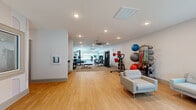 Located at 3017 Old Amy Rd in Laurel, Mississippi, this single-floor fitness facility offers a thoughtfully designed layout dedicated to health and wellness. The space comprises two exercise rooms, a private office, and two bathrooms, all finished with clean, modern aesthetics.

The primary exercise area features warm bamboo hardwood flooring and is outfitted with a diverse array of strength and conditioning equipment, including a power rack with free weights, benches, cable machines, and a wall-mounted dumbbell rack. A dedicated rack holds an assortment of exercise balls and resistance bands, while a comfortable seating area provides a space to rest between sessions. Recessed lighting and ceiling fans keep the environment bright and comfortable.

The second exercise room is carpeted and bathed in natural light through expansive floor-to-ceiling windows that overlook a lush outdoor landscape. This room houses cardio equipment including treadmills, ellipticals, stationary bikes, and a rowing machine, all positioned to take advantage of the scenic outdoor views.

The private office is compact and functional, featuring light hardwood flooring, a large interior window, and a clean workspace. Both bathrooms are finished with classic white subway tile walls, mosaic tile flooring, and accessibility-friendly fixtures. Together, these spaces form a comprehensive and well-appointed fitness facility.