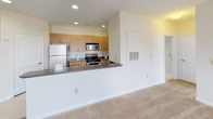 This single-floor residence offers a practical and comfortable layout designed for everyday living. The open-concept kitchen is a functional highlight, featuring warm wood cabinetry, dark granite-style countertops, and a full suite of stainless steel appliances including a refrigerator, range, and over-the-range microwave. A peninsula counter provides additional workspace and visually connects the kitchen to the adjacent living area, which is finished with plush wall-to-wall carpeting and a ceiling fan overhead. Multiple windows fitted with horizontal blinds allow natural light to flow through the space while offering views of the surrounding greenery. A glass-panel door in the living area provides direct access to the outdoors. The bedrooms are generously proportioned, each featuring soft carpeting, large windows with natural light, and neutral wall tones that lend a clean, airy feel. The bathroom is well-equipped with a full vanity featuring white cabinetry and a dark granite countertop, a large wall mirror, and a tub-shower combination. Tile flooring in the kitchen and bathroom contrasts with the warm carpeting throughout the rest of the unit, creating a cohesive yet practical design. Recessed lighting in the kitchen and consistent neutral tones throughout contribute to a bright and welcoming ambiance.