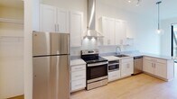 Located at 100 N First St in the heart of Minneapolis, MN, this modern single-floor unit offers a thoughtfully designed layout with clean, contemporary finishes. The open-concept kitchen is a standout feature, equipped with stainless steel appliances including a refrigerator, range with microwave, and dishwasher. White shaker-style cabinetry provides ample storage, complemented by light quartz countertops, a stainless steel sink, and a sleek wall-mounted range hood. Open floating shelves and a globe pendant light add a stylish, modern touch. The kitchen flows seamlessly into the living area, where light hardwood flooring and floor-to-ceiling windows invite abundant natural light and frame urban views of the Minneapolis skyline. A ceiling fan enhances comfort in the main living space. The bedroom is a bright, minimalist room with direct access to a private balcony through a large window, offering additional city views. The bathroom features white subway tile surrounding a soaking tub and shower, grey tile flooring, a white vanity with quartz countertop, and warm wood-framed mirrors and trim. A hallway connects the main living areas to the bathroom and entry, maintaining a clean and efficient flow throughout the unit.