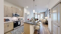 This single-floor, 2-bedroom, 2-bathroom residence features a contemporary open-concept design that seamlessly connects the kitchen, dining, and living areas. The kitchen is a standout, equipped with light wood cabinetry, dark granite countertops, stainless steel appliances including a refrigerator and range, and a central island with bar seating illuminated by stylish pendant lighting — ideal for both cooking and casual dining. Wood-style flooring flows throughout the main living areas, enhancing the warm, modern aesthetic.

The living room is bright and inviting, featuring large windows that welcome ample natural light and a ceiling fan for comfort. Both bedrooms offer a serene retreat, highlighted by soft blue accent walls, generous windows with outdoor views, and plush carpeting. Each bedroom is served by a dedicated closet with built-in shelving and hanging storage, providing practical organization solutions.

The primary bathroom features a dual-sink vanity with wood cabinetry and stone countertops, a soaking tub, and direct access to a walk-in closet. The second bathroom maintains the same refined design language. Throughout the residence, clean white walls, neutral tones, and consistent finishes create a cohesive and modern living environment.