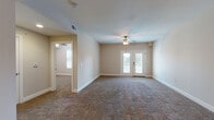 This single-floor residence offers a thoughtfully designed layout that balances comfort and functionality throughout. The open-concept kitchen serves as a central hub, featuring rich dark wood cabinetry, white countertops, stainless steel appliances including a refrigerator, electric range with microwave, and dishwasher. A peninsula island with pendant lighting overhead provides additional prep space and defines the transition into the adjoining living area, which is finished with neutral-toned tile flooring.

The spacious living room is carpeted in a warm, neutral tone and is highlighted by a ceiling fan with light fixture. French doors lead out to an exterior balcony or patio, allowing natural light to fill the room and offering outdoor views. An additional connected room, also carpeted and equipped with a ceiling fan, provides flexible space for a secondary living or dining area.

The bedrooms are generously sized, each featuring plush carpet, ceiling fans, and natural light through window blinds. One bedroom includes a double-door closet for ample storage. Both bathrooms are finished with tile flooring and warm wood vanities with white countertops. The primary bathroom includes a walk-in shower with a glass sliding door and tiled surround, while the secondary bathroom features a single vanity and toilet.