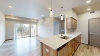 Located at 205 S Pines Rd in Spokane Valley, WA, this 2-bedroom, 1-bathroom unit offers a thoughtfully designed open-concept layout with modern finishes throughout. The combined kitchen and living area serves as the heart of the unit, featuring light wood-tone cabinetry, stainless steel appliances including a refrigerator, range, and microwave, and a central island with a white quartz countertop and undermount sink. Pendant lighting above the island adds a contemporary touch, while light wood-style flooring and recessed ceiling lights contribute to a clean, bright aesthetic. A wall-mounted mini-split system provides efficient climate control. Sliding glass doors open onto a private balcony, bringing in natural light and outdoor views. The living area is spacious and open, continuing the light flooring and neutral palette. Both bedrooms feature plush carpeting, windows for natural light, and wall-mounted mini-split units. The primary bedroom includes a walk-in closet with wire shelving for ample storage. The full bathroom is well-appointed with a wood-tone vanity, white countertop, a tub-shower combination, and an adjacent built-in linen cabinet. A dedicated hallway with convenient entry access completes this efficiently organized and contemporary unit.