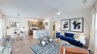 This single-floor residence is designed with a clean, modern aesthetic and an open-concept layout that seamlessly connects the living, dining, and kitchen areas. The living room is bright and welcoming, featuring wood-look flooring, a ceiling fan with integrated lighting, and large windows that fill the space with natural light and offer outdoor views. The kitchen is well-appointed with flat-front wood-toned cabinetry, stainless steel appliances including a refrigerator, microwave, and electric range, and a white quartz peninsula with an undermount sink and seating for casual dining. Track lighting overhead adds focused illumination throughout the kitchen.

The bedrooms are generously sized, each featuring plush carpeting, ceiling fans, and large windows that bring in ample natural light with views of surrounding greenery. The rooms provide a calm, restful atmosphere with neutral wall tones and ample space for furniture.

The bathroom maintains the home's contemporary style, finished in crisp white with a tiled tub-shower combination, built-in open shelving for storage, and clean, simple fixtures. Throughout the residence, a consistent palette of white walls, warm wood accents, and modern finishes creates a cohesive and inviting living environment.