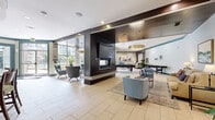 Located at 1055 Pine St in Nashville, TN, this well-appointed community amenity space offers a sophisticated and welcoming environment across a single, expansive floor. The open-plan layout is anchored by a striking dark-paneled fireplace column, which also houses a large flat-screen TV, serving as a natural divider between distinct functional zones while maintaining a cohesive, flowing design.

Light-toned large-format tile flooring runs throughout, lending the space a clean and modern aesthetic. Teal accent trim and door frames add a bold, consistent design thread that ties each area together. Seating areas are thoughtfully arranged, featuring plush sofas, accent chairs in shades of blue and tan, and layered area rugs that define intimate gathering spots.

A dedicated game area includes a full-sized billiards table, while a cozy media nook provides wall-mounted TV viewing alongside a built-in fireplace and comfortable lounge chairs. The wet bar area is highlighted by a curved countertop with bar seating, pendant lighting, mosaic tile backsplash, and dark cabinetry — ideal for entertaining.

Large windows along the perimeter flood the space with natural light and provide views of the surrounding Nashville streetscape. The overall ambiance is polished yet comfortable, blending contemporary design with inviting, social-centered functionality.