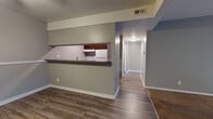 Located at 501 W 27th St S in Wichita, Kansas, this single-floor unit offers a practical and well-organized layout designed for comfortable everyday living. The living area is generously sized, featuring warm carpet flooring and a large sliding glass door fitted with vertical blinds that allows abundant natural light to fill the room. A ceiling fan adds to the comfort of the space.

The kitchen is efficiently arranged in a galley style, showcasing rich dark cabinetry, laminate countertops, a double-basin sink, and white appliances including a range and refrigerator. Wood-look vinyl flooring runs throughout the kitchen and connecting hallway. A pass-through counter opening connects the kitchen to the main living area, creating an open and communicative flow between spaces.

Multiple bedrooms are present, each finished with plush carpet, neutral gray walls, ceiling fans with light fixtures, and individual windows with blinds that bring in natural light. The bathroom features a full-size soaking tub and shower combination with white tile surround and wood-look flooring. A central hallway connects all rooms efficiently. Textured ceilings are consistent throughout, and the overall color palette of soft grays and warm neutrals gives the unit a clean, move-in ready appearance.