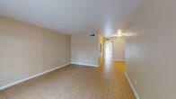 This single-floor unit offers a practical and straightforward layout with a consistent design language throughout. Light beige tile flooring extends across all living areas, providing a clean and cohesive look that is easy to maintain. The walls are painted in warm, neutral tones that create a welcoming atmosphere and complement the tile underfoot.

The main living area is generously proportioned, with smooth ceilings fitted with ventilation registers ensuring comfortable climate control. A hallway connects the living spaces to the additional rooms, maintaining a logical and efficient flow throughout the unit.

One of the standout features is a room with a sliding glass door that opens to an outdoor area, allowing natural light to pour in and offering a pleasant view of surrounding greenery. This connection to the outdoors adds an airy quality to the interior.

The bathroom is well-appointed with a full tub-and-shower combination, a toilet, and a vanity featuring white cabinetry, a granite-style countertop, a single basin sink, and a large mirror with overhead lighting. A dedicated laundry area accommodates a stacked washer and dryer unit, adding significant convenience. White baseboards throughout the space provide a clean, finished appearance.