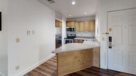 Located at 1500 E Kilgore Rd in Portage, Michigan, this single-floor, one-bedroom, four-bathroom unit offers a well-organized and functional layout. Rich, dark hardwood-style flooring runs throughout the main living areas, creating a warm and cohesive aesthetic. The open-concept living, dining, and kitchen area is bright and airy, with multiple windows allowing natural light to fill the space. Ceiling fans in the living area and bedroom provide added comfort. The kitchen is thoughtfully designed with warm wood cabinetry, granite-style countertops, a peninsula with bar seating, and a full suite of stainless steel appliances including a refrigerator, range, microwave, and dishwasher. The bedroom features two windows with outdoor views of surrounding greenery, providing a peaceful retreat. Three closets offer generous storage throughout the unit. The four bathrooms are finished with light tile flooring, granite-topped vanities with wood cabinetry, and tub/shower combinations with white tile surround. Clean white walls, recessed lighting in the kitchen, and a textured ceiling in the main living area round out the interior details, giving the unit a tidy and move-in-ready appearance.