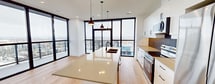 This contemporary 760 square foot apartment offers a blend of style and functionality. The space boasts two bedrooms, including a primary bedroom of 150 square feet, and two full bathrooms. Floor-to-ceiling windows dominate the living areas, flooding the space with natural light and providing breathtaking panoramic city views.

The open-concept kitchen is a highlight, featuring sleek white cabinetry, stainless steel appliances, and a distinctive textured backsplash. A generous island with a light-colored countertop serves as both a prep area and casual dining space. The living room seamlessly connects to a private balcony, perfect for enjoying the urban vistas.

Both bathrooms exhibit modern design, with one showcasing a wooden vanity, round mirror, and glass-enclosed shower. The bedrooms are well-proportioned, with ample closet space and continuation of the warm hardwood flooring found throughout the apartment.

The unit's design maximizes space efficiency, with clean lines and a neutral color palette enhancing the sense of openness. Recessed lighting and strategically placed pendant lights add to the contemporary ambiance. Located at 110 Fullarton, this high-rise apartment offers the perfect blend of urban living and comfort.