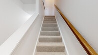 This three-floor home offers a practical and comfortable layout across three levels. The ground floor houses an attached garage with a concrete floor and utility room, providing convenient storage and functional support space. A staircase with carpet-covered treads and a warm wood handrail connects each level seamlessly.

The main living floor is the heart of the home, featuring an open-plan kitchen and living area filled with natural light from a sliding glass door that leads to an outdoor balcony. The kitchen is well-equipped with dark espresso cabinetry, granite countertops, stainless steel appliances including a refrigerator, range, microwave, and dishwasher, and a central island with additional counter space. Wood-look flooring runs throughout, complementing the clean, modern aesthetic. A half bath with a pedestal sink adds convenience on this floor.

The upper floor is dedicated to the three bedrooms, including a generously sized primary bedroom, along with two full bathrooms. The bedrooms feature plush carpeting, natural light from windows with blinds, and access to closets. The bathrooms are finished with tile flooring, dark vanity cabinetry, and mirrors. A hallway with a wood-railed staircase connects the upper level, maintaining the home's consistent, clean design throughout.