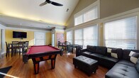 Located at 3530 Brookstone Dr in Cincinnati, Ohio, this single-floor space is designed with entertainment and comfort in mind. The open layout is anchored by dramatic vaulted ceilings that rise to impressive heights in the main gathering area, creating a sense of spaciousness enhanced by large, multi-pane windows dressed with horizontal blinds that allow generous natural light to flood the warm hardwood floors throughout.

The main lounge area features a large sectional leather sofa with matching ottoman, providing ample seating for groups. Adjacent to the lounge, a dedicated game area includes a full-sized pool table and a foosball table, making the space well-suited for social gatherings. A dining nook with a raised pub-style table and chairs sits near glass-panel French doors, and a wall-mounted flat-screen television adds a media component to the area.

The kitchen is outfitted with rich dark espresso cabinetry, granite countertops, a white subway tile backsplash, stainless steel appliances including a refrigerator and microwave, and a double sink — offering full functionality. Crown molding, yellow accent walls, and decorative artwork contribute to the space's inviting, lively ambiance throughout.