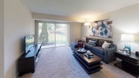 This single-floor residence offers a thoughtfully designed layout that balances comfort and functionality throughout its well-defined spaces. The living room serves as the heart of the home, featuring plush wall-to-wall carpeting, neutral walls, and large sliding glass doors fitted with vertical blinds that flood the space with natural light and provide direct views of the surrounding greenery outside. The open, carpeted living area provides generous room for seating and entertainment.

The kitchen is equipped with warm honey-toned wood cabinetry offering ample storage, granite-style countertops, and a full suite of stainless steel appliances including a gas range, dishwasher, and refrigerator. Tile flooring adds practicality to this functional cooking space.

The bedroom is a serene retreat, carpeted and bathed in natural light from a window, with wall space accommodating decorative artwork. A generously sized reach-in closet with built-in shelving provides substantial storage. The adjoining bathroom features a white vanity with an integrated sink and a mirrored medicine cabinet.

A second full bathroom with tile flooring, a white vanity, and clean, bright finishes serves the remainder of the residence. Throughout, the neutral color palette and consistent finishes create a cohesive and welcoming ambiance.