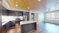 This thoughtfully designed single-floor unit blends modern aesthetics with functional living. A standout architectural feature is the natural wood-plank ceiling that spans the kitchen and living areas, adding warmth and texture to the otherwise clean, contemporary palette. Recessed lighting and ceiling fans complement the design throughout.

The kitchen is a highlight, outfitted with sleek charcoal-gray cabinetry, white quartz countertops, a full suite of stainless steel appliances including a refrigerator, range, and over-the-range microwave, a white tile backsplash, and a central island that doubles as a prep and dining space. Wood-look flooring flows seamlessly through the kitchen and into the living areas.

Two well-proportioned bedrooms feature plush carpeting, large windows with views of the surrounding neighborhood, individual ceiling fans, and wall-mounted mini-split units for climate control. The primary bedroom includes a spacious walk-in closet with built-in wire shelving.

Two full bathrooms serve the unit, each finished with wood-look flooring, white quartz vanities, and a tub-shower combination with white subway tile surround. One bathroom features built-in open shelving for additional storage. Completing the layout is a dedicated in-unit laundry area, adding everyday convenience to this well-appointed space.