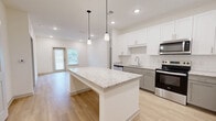 Located at 1485 Fouraker Rd in Jacksonville, FL, this single-story, 3-bedroom, 2-bathroom home offers a thoughtfully designed layout with modern finishes throughout. The open-concept kitchen and dining area serves as the heart of the home, anchored by a large granite-topped island with pendant lighting above. White shaker upper cabinets contrast with gray lower cabinets, complemented by a classic subway tile backsplash and a full suite of stainless steel appliances, including a refrigerator with ice and water dispenser, range, microwave, and dishwasher. Light hardwood-style flooring extends through the main living areas, creating a bright and cohesive aesthetic. The living room flows naturally from the kitchen, bathed in natural light from a windowed door. Each of the three bedrooms features plush carpet flooring, windows with blinds, and ceiling fans for comfort. The primary bedroom includes a walk-in closet outfitted with wire shelving for ample storage. The bathrooms are finished with granite-topped vanities, white cabinetry, dark-framed mirrors, and clean tile work. Additional highlights include a dedicated laundry area, a hallway connecting the bedrooms, and four closets throughout for generous storage capacity.