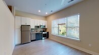 Located at 530 N Patterson Ave in Winston-Salem, NC, this single-floor unit offers a clean, modern design with thoughtful finishes throughout. The kitchen is a standout feature, equipped with stainless steel appliances including a full-size refrigerator, dishwasher, microwave, and range. White upper cabinetry pairs with dark lower cabinets, creating a two-tone aesthetic complemented by a mosaic tile backsplash and granite-style countertops. A large window floods the kitchen and adjacent living area with natural light, offering views of surrounding greenery. Light wood-tone vinyl plank flooring runs seamlessly throughout the entire unit, contributing to a cohesive and contemporary feel. The living area is open and well-proportioned, with neutral warm beige walls and ceiling fans providing functional comfort. A dedicated bedroom area features the same consistent flooring and neutral palette, with ample wall outlets for flexible furniture arrangement. The bathroom is neatly appointed with a dark-toned vanity, granite countertop, and durable plank flooring, with accessibility-friendly grab bar support. Recessed lighting and well-placed ventilation throughout the unit ensure a comfortable and well-lit environment year-round.