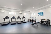 Located at 300 Riverfront Boulevard in Elmwood Park, NJ, this single-floor amenity space offers a thoughtfully designed environment that balances social comfort with active wellness. The centerpiece is a striking double-height lounge area defined by soaring ceilings and an expansive band of clerestory windows that flood the space with abundant natural light. Crisp white walls, large-format gray tile flooring, and contemporary leather seating arrangements create a sleek, modern aesthetic throughout. A wall-mounted flat-screen TV and open sightlines contribute to a welcoming, communal atmosphere, while glass-panel partitions elegantly divide areas without sacrificing the sense of openness.

The fitness center is generously proportioned and comprehensively equipped, featuring multiple treadmills, a stationary bike, an elliptical, a power rack, cable machines, free weights, kettlebells, and a dedicated functional training area with a heavy bag and medicine balls. Rubber flooring, recessed lighting, wall-to-wall mirrors, and independent climate control units ensure a comfortable and practical workout environment.

Two ADA-compliant bathrooms complete the space, each outfitted with floating dark-granite vanities, large mirrors, grab bars, and clean white tile — maintaining the modern design language found throughout the facility.