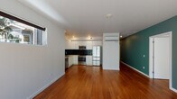 Located in Portland's desirable Northwest neighborhood, this modern single-floor unit at 2330 NW Raleigh St offers a well-designed open layout with warm hardwood flooring throughout. The living area is bathed in natural light, courtesy of large floor-to-ceiling windows and additional clerestory windows that frame lush greenery views, creating a seamless indoor-outdoor connection.

The kitchen is a standout feature, outfitted with sleek white cabinetry, a bold black subway tile backsplash, white quartz countertops, and a full suite of stainless steel appliances including a gas range, microwave, French door refrigerator, and dishwasher. A wall-mounted mini-split unit provides efficient climate control throughout the space.

A teal accent wall adds a striking pop of color to the main living zone, which flows effortlessly into the hallway corridor leading to the bedrooms. The bedrooms are bright and clean, each featuring hardwood floors and natural light from well-placed windows. The bathroom is finished with white tile wainscoting, a wide vanity with ample cabinetry, an oversized mirror, and a combination tub and shower. The overall aesthetic is clean, contemporary, and move-in ready.