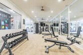 Located in Columbus, GA, this fitness facility is a thoughtfully designed, single-floor space built to support a full range of workout routines. The gym is finished with neutral gray walls, crown molding, and durable carpet-tile flooring that lends a clean, polished aesthetic throughout.

The strength training area is expansive and well-appointed, featuring power racks, cable machines, adjustable benches, and a comprehensive dumbbell rack. Full-length mirrors line the walls, visually expanding the space and allowing users to monitor their form during workouts. Recessed lighting provides consistent, bright illumination across the entire floor.

The cardio zone is anchored by a row of TRUE-brand treadmills and includes a rowing machine and additional cardio equipment. Large windows along one wall invite natural light and offer views of the surrounding greenery, creating an energizing atmosphere. Ceiling fans add to the comfort of the space during intense sessions.

Workout reference charts and instructional posters are mounted on the walls, adding a functional and educational element to the environment. A dedicated children's area, labeled "Greystone Kids," is visible along one wall, making this a family-friendly fitness destination. The overall layout is spacious and organized, ensuring ample room for movement and safe use of all equipment.