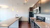 Located in Denver's vibrant Capitol Hill neighborhood, this one-bedroom, one-bathroom residence offers a well-designed layout across a single floor. The open-concept kitchen and living area serves as the heart of the home, featuring rich dark hardwood flooring, dark-finish cabinetry, granite countertops, a subway tile backsplash, and a full suite of stainless steel appliances including a refrigerator, range, and microwave. A peninsula with an undermount sink and pendant lighting above adds both function and style, flowing seamlessly into the living space. The bedroom is a comfortable, carpeted retreat with access to a private balcony through sliding glass doors, framing views of the surrounding Denver cityscape and allowing abundant natural light to fill the room. An additional window further brightens the space. The bathroom is clean and modern, finished with wood-look flooring, a granite-topped vanity, dark cabinetry, and a glass-enclosed walk-in shower with white tile surround. A dedicated closet provides practical storage. Track lighting and pendant fixtures throughout contribute to the contemporary aesthetic of this efficiently designed Denver residence.