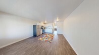 La Modera B22 is a well-designed one-bedroom, one-bathroom residence located in Federal Way, WA. The open-concept layout seamlessly connects the living area and kitchen, creating a bright and functional living space. Wide-plank wood-style flooring runs throughout the main living and kitchen areas, lending a clean, contemporary feel.

The kitchen is thoughtfully equipped with stainless steel appliances, including a full-size refrigerator and electric range, complemented by crisp white cabinetry that extends to the upper walls for ample storage. A sink and additional counter space complete the functional workspace. Natural light filters into the kitchen and living area through a large window, offering views of surrounding greenery.

The bedroom is a comfortable, private retreat finished with plush wall-to-wall carpeting. A large window allows natural light to fill the room, and a wide sliding double-door closet provides generous storage. Baseboard heating is present throughout the unit.

The bathroom features a white vanity with a large mirror, a combination tub and shower with a decorative curtain, and wood-style flooring that ties the space together with the rest of the home. Clean white walls and brushed nickel hardware give the bathroom a fresh, modern appearance. Overall, this residence offers a practical and inviting layout suited for comfortable everyday living.
