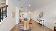 This two-story home is designed with a clean, contemporary aesthetic, characterized by white walls, light wood-look flooring, and recessed lighting that create a bright and welcoming atmosphere throughout. The open-concept main living area seamlessly connects the dining space and kitchen, promoting an effortless flow between rooms. The kitchen is well-appointed with white shaker cabinetry, a subway tile backsplash, light-toned countertops, stainless steel appliances including a French door refrigerator, a built-in microwave, and a range. A central island with an undermount sink provides additional workspace and casual seating. The dining area comfortably accommodates a full-sized table and is positioned adjacent to a white sideboard, adding practical storage. The living room offers natural light through a window with views of surrounding greenery. Bedrooms are generously sized, featuring closets and continuing the consistent wood-look flooring. The full bathroom includes a wide vanity with stone-look countertops, ample cabinet storage, a large mirror, and a walk-in shower. A convenient powder room with a pedestal sink serves the main level. A dedicated laundry room with side-by-side washer and dryer completes the home's practical layout.