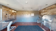 Located at 7555 E Warren Dr in Denver, Colorado, this pet spa is a purpose-built grooming facility designed with both functionality and character in mind. The single-room space makes efficient use of its compact footprint, offering a thoughtfully organized environment for professional pet care. The interior features rich, warm wood-plank accent walls that provide a rustic contrast against the cool gray painted surfaces, creating an inviting yet practical atmosphere. Playful paw print decals adorn the walls, reinforcing the space's pet-friendly identity. The stained concrete flooring is durable and easy to clean, complemented by rubber anti-slip matting throughout the work areas for added safety. A stainless steel wash tub with an integrated ramp is positioned along one wall, alongside an adjustable hydraulic grooming table, providing professional-grade equipment for grooming services. A wall-mounted mini-split HVAC unit ensures year-round climate control. The entry area features a glass-paneled door flanked by windows that allow natural light to filter into the space and offer views of the parking area. Recessed ceiling lighting and ceiling-mounted speakers complete the well-appointed interior, creating a comfortable and efficient environment for pets and groomers alike.