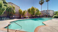 Located at 1660 Drew Cir in Davis, California, this expansive outdoor amenity area serves as the social and recreational heart of the community. The centerpiece is a generously sized swimming pool with a smooth concrete surround, flanked by rows of navy blue cushioned chaise lounges and green reclining chairs that invite relaxation under the abundant California sun. Towering palm trees and sweeping weeping willows frame the space, providing both shade and a lush, resort-like atmosphere.

Adjacent to the main pool is a dedicated spa area, complete with stainless steel handrails and additional seating for quiet unwinding beneath the canopy of mature trees. A covered lounge pavilion, supported by substantial concrete columns, offers a shaded retreat with comfortable seating that overlooks the pool deck.

The outdoor kitchen and BBQ area is a standout feature, equipped with built-in grills set within stone-clad structures alongside casual seating — ideal for outdoor gatherings. Manicured garden beds, colorful planters, and well-maintained shrubbery line the walkways, adding vibrant greenery throughout. Ornamental lamp posts and secure gated access complete the thoughtfully designed landscape, creating a welcoming and functional outdoor environment.