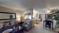 This single-floor, 1-bedroom, 1-bathroom residence delivers a thoughtfully organized layout that maximizes functionality and comfort. The open living area features plush carpeting, neutral-toned walls, and a textured ceiling, creating a warm and inviting atmosphere. A large sofa, accent chair, and decorative mirror anchor the space, while a pass-through window connects the living room seamlessly to the kitchen, enhancing the sense of openness. The galley-style kitchen is efficiently designed with ample light wood cabinetry, generous counter space, a double-basin sink, and white appliances including a range and refrigerator, making it well-suited for everyday cooking. The bedroom is a comfortable retreat, featuring soft carpeting, a ceiling fan with light fixture, and a walk-in closet that provides excellent storage. The room accommodates a full-sized bed with ease and includes additional closet access. The bathroom is equipped with a wide vanity countertop featuring dual sinks, a large wall mirror with Hollywood-style lighting, and a clean, bright tub and shower enclosure. Throughout the residence, the neutral color palette and consistent flooring choices contribute to a cohesive and practical living environment.