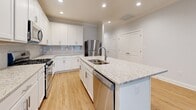 This single-story, 3-bedroom, 2-bathroom home offers a thoughtfully designed layout with a seamless blend of modern finishes and functional living spaces. The open-concept kitchen and living area serves as the heart of the home, featuring a large center island with granite countertops and a double sink, white shaker-style cabinetry, a blue tile backsplash, and a full suite of stainless steel appliances including a gas range, built-in microwave, refrigerator, and dishwasher. Light hardwood flooring flows throughout the main living areas, complemented by recessed lighting and a ceiling fan. The spacious primary bedroom includes crown molding, a ceiling fan, and direct access to a private en-suite bathroom with a glass-enclosed walk-in shower and tile flooring, as well as a generous walk-in closet outfitted with wire shelving. Two additional bedrooms feature plush carpet, natural light from bright windows, and clean white panel doors. The secondary bathroom includes a full tub/shower combination, granite vanity, and tile flooring. A dedicated hallway and closet complete the layout, offering practical storage solutions throughout this clean and move-in-ready home.