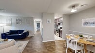 This single-floor residence offers a thoughtfully designed layout that connects key living areas with ease. The living room serves as the heart of the home, featuring wood-look flooring, a textured ceiling, and a sliding glass door that opens onto a private balcony overlooking a lush, tree-lined backdrop — filling the space with natural light and greenery. Adjacent to the living room, the dedicated dining area accommodates a round table setup and features matching wood-look floors, neutral gray walls with a chair rail detail, and overhead lighting. The galley-style kitchen is efficiently organized with dark cabinetry, white tile countertops, a subway tile backsplash, stainless steel appliances including a range and refrigerator, and tile flooring — offering ample storage through upper and lower cabinets. A hallway connects the common areas to the private quarters, leading to a generously sized bedroom carpeted for comfort, with a walk-in closet providing excellent storage. The full bathroom features wood-look flooring, a dark vanity with a white countertop, and a tub-shower combination. A utility area houses the HVAC system and electrical panel, completing this practical and comfortable single-level home.