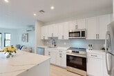 Located at 6 Rantoul Street in Beverly, MA, this thoughtfully designed 2-bedroom, 3-bathroom residence offers a clean, modern aesthetic across a single floor. The open-concept kitchen and living area serves as the heart of the home, featuring crisp white shaker cabinetry, a striking veined quartz waterfall island with bar seating, subway tile backsplash, stainless steel appliances, and a matte black faucet — all set above light-toned hardwood flooring that flows throughout the space. The living room is bright and airy, with large black-framed windows inviting natural light and a wall-mounted mini-split system for year-round comfort. The spacious primary bedroom offers a calm, neutral palette, ample room, and its own mini-split unit. A second well-proportioned bedroom provides flexibility for guests or a home office. The three bathrooms are finished with contemporary fixtures, including a sleek glass-enclosed walk-in shower with large-format white tile and matte black hardware, as well as a full bath with tub. An additional flex space with glass-paned doors adds versatility to the layout. Recessed lighting, clean lines, and a cohesive light-and-white color palette give the entire residence a fresh, modern feel.