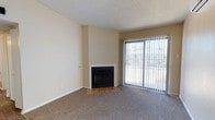 This single-story residence offers a practical and comfortable layout across several well-defined spaces. The living room serves as a central gathering area, showcasing a corner fireplace with a tile hearth set against neutral-toned walls and plush carpeting. A full-height sliding glass door fitted with vertical blinds allows ample natural light and provides outdoor access. A wall-mounted mini-split air conditioning unit near the entryway ensures efficient climate control, while wood-look laminate flooring transitions from the carpeted living area near the front door.

The kitchen is equipped with dark espresso cabinetry, light countertops, a white electric coil range, and a range hood overhead. A refrigerator is also included, and the layout offers functional counter space throughout.

The bedrooms are carpeted and feature ceiling fan-light fixtures and windows with blinds that bring in natural light. One bedroom connects directly to a full bathroom featuring a wide vanity with dark cabinetry, a large mirror, and a separate water closet. A second bathroom includes a tub-shower combination, a medicine cabinet, and built-in shelving. Textured ceilings are consistent throughout the home, contributing to a cohesive aesthetic.