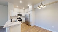 This single-floor residence is designed with a clean, contemporary aesthetic throughout. The open-concept living and dining area serves as the heart of the home, featuring light hardwood-style flooring, neutral gray-toned walls, and a ceiling fan with an integrated light fixture. A chandelier pendant adds a decorative touch above the dining space, while a pass-through peninsula connects seamlessly to the kitchen. A dedicated laundry area is accessible directly from the main living space.

The kitchen is well-equipped with white shaker-style cabinetry, light quartz countertops, recessed lighting, and a full suite of stainless steel appliances including a French door refrigerator, electric range, over-the-range microwave, and dishwasher. Hardwood-style flooring continues throughout this space.

The bedrooms are carpeted for comfort and each include ceiling fans and windows with blinds that allow natural light while maintaining privacy. One bedroom features access to a walk-in closet with built-in shelving and hanging rods.

The bathroom includes a white vanity with a quartz countertop, a tub-shower combination with tiled surround, and bronze-toned fixtures, all complemented by hardwood-style flooring and a window for natural ventilation.