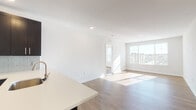 Located at 100 Town Center Blvd in Sewell, NJ, this single-floor unit offers a clean, modern aesthetic throughout. The open-concept layout seamlessly connects the kitchen and living area, creating a spacious and functional flow. The kitchen is a standout feature, equipped with stainless steel appliances including a refrigerator, range, and microwave, complemented by dark espresso cabinetry, a light glass tile backsplash, white quartz countertops, and a peninsula with a built-in sink — ideal for both cooking and casual dining. Wood-style plank flooring runs throughout the main living areas, adding warmth to the contemporary design. The living room is bathed in natural light from large windows that frame views of the surrounding community. A private bedroom features a sliding glass door with vertical blinds, allowing additional natural light and outdoor access. The bathroom is well-appointed with a double-sink vanity set in dark cabinetry, a wide framed mirror, white quartz countertops, and a full tiled tub-shower combination. Crisp white walls and recessed lighting throughout contribute to a bright, airy ambiance, making this a polished and move-in ready space.