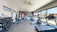 Located in Tucson, Arizona, this dedicated fitness center offers a thoughtfully designed exercise space that combines functionality with motivating aesthetics. The room is finished with durable speckled rubber flooring, providing a safe and supportive surface throughout the workout area.

A striking feature of the space is the dramatic dark accent wall adorned with large-scale athletic murals, creating an energizing atmosphere that encourages peak performance. Ceiling fans are installed overhead to promote air circulation, complementing the recessed lighting that keeps the space bright and well-lit.

The fitness center is comprehensively equipped for a full-body workout. Cardio equipment includes Spirit-brand treadmills and elliptical trainers, along with stationary and cycling bikes. Strength training is well-represented with a multi-functional cable and weight machine, a full rack of dumbbells with an adjustable bench, and a collection of stability and medicine balls for functional fitness exercises.

Large floor-to-ceiling windows line one wall, inviting abundant natural light and framing views of the surrounding Tucson landscape and distant mountain silhouettes. A set of glass double doors opens to an outdoor patio area, further connecting the interior to the scenic desert environment. The overall design is modern, clean, and purpose-built to support a wide range of fitness routines.