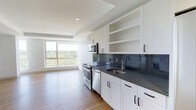 This well-appointed 1-bedroom, 1-bathroom residence offers a clean, modern aesthetic throughout its single-floor layout. The open-concept kitchen and living area is anchored by a sleek kitchen featuring white shaker-style cabinetry with matte black hardware, dark subway tile backsplash, and dark countertops that provide a striking contrast. Stainless steel appliances, including a range, microwave, and dishwasher, complete the functional and stylish culinary space. Open shelving adds a contemporary touch and provides additional display and storage options. The kitchen flows seamlessly into the living area, which is bathed in abundant natural light streaming through large floor-to-ceiling windows. These expansive windows frame beautiful treetop and greenery views, creating a bright and airy ambiance throughout. Warm hardwood-style flooring runs continuously through the space, adding warmth and cohesion to the overall design. Recessed lighting and crisp white walls further enhance the clean, contemporary feel of the residence. The combination of modern finishes, natural light, and scenic views makes this a comfortable and visually appealing living space.