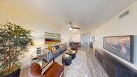 This thoughtfully designed single-floor residence offers two bedrooms and one bathroom across a comfortable and efficiently utilized floor plan. Light wood-tone flooring flows consistently throughout, creating a cohesive aesthetic from room to room.

The living room is anchored by a ceiling fan and opens directly to a private outdoor area through sliding glass doors, flooding the space with natural light. The open-concept layout connects the living room to a dedicated dining area, which features a rustic wood dining table beneath a striking industrial-style pendant light.

The kitchen is accessed via a pass-through counter with bar seating, ideal for casual dining. It is equipped with stainless steel appliances, including a full-size refrigerator, microwave, and range, complemented by white cabinetry and clean countertops.

The primary bedroom is generously proportioned, featuring a ceiling fan, natural light from a window, and direct access to a closet. The second bedroom offers a similar layout with its own closet access. A dedicated closet area with built-in shelving provides additional storage.

The bathroom is finished with marble-style tiled walls surrounding a full tub-shower combination, paired with a white vanity, quartz countertop, and a large mirror. Clean white walls and wood-look flooring carry the home's modern aesthetic throughout.