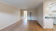 Located at 10853 Firestone Blvd in Norwalk, CA, this one-bedroom, one-bathroom unit offers a well-organized single-floor layout designed for efficient, comfortable living. The interior is finished with warm wood-look flooring throughout, complemented by neutral beige walls and crisp white trim and crown molding that lend a clean, cohesive aesthetic.

The living room is open and airy, benefiting from natural light streaming in through a large window with horizontal blinds. Crown molding adds a refined detail to the space, while a wall-mounted climate unit and a ceiling fan with light fixture provide year-round comfort. A front entry door with a transom window enhances the brightness of the room.

The galley-style kitchen is efficiently designed with white cabinetry lining both sides, offering ample storage. It features white countertops, a stainless steel sink, and black appliances including a gas range with overhead microwave and a refrigerator. Light wood-look flooring and overhead flush lighting complete the functional space.

The bedroom is a comfortable, sun-lit room with a window, a wall-mounted AC unit, a ceiling fan, and access to a built-in closet. The bathroom includes a full tub-shower combination with chrome fixtures and a small window above for natural ventilation. A closet with bi-fold doors is also accessible from the hallway area.