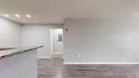 This 910-square-foot, one-bedroom, one-bathroom apartment in Peabody, MA offers a thoughtfully designed single-floor layout. The combined kitchen and living room serves as the heart of the unit, featuring durable wood-look flooring and neutral gray walls throughout. The kitchen is outfitted with rich dark wood cabinetry, granite countertops, and a full suite of stainless steel appliances, including a gas range, refrigerator, dishwasher, and microwave. The open living area benefits from abundant natural light through large windows with views of surrounding greenery. The 140-square-foot bedroom is a comfortable retreat, complete with a ceiling fan, a window overlooking outdoor trees, and direct access to a closet. The bathroom features a full tub-shower combination with tiled surround, and a clean, neutral palette. A dedicated in-unit laundry room includes a full-size washer and dryer with wire shelving above for additional storage. The unit also includes a hallway and entrance area, contributing to a practical and well-organized floor plan. Clean lines, consistent flooring, and a cohesive neutral color scheme give this apartment a modern, move-in-ready feel.