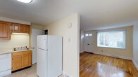 This 2-bedroom, 1-bathroom residence is spread across three floors, offering a practical and comfortable layout. The kitchen is equipped with standard appliances, including a full-size refrigerator, and features tile flooring that transitions seamlessly into the adjoining living areas. Light-toned walls throughout create a bright and airy atmosphere, contributing to the home's clean, neutral aesthetic. The entryway is highlighted by a classic paneled front door with transom windows above, allowing natural light to filter into the space and illuminate the warm hardwood floors that extend through the main living area. Baseboard heating is present, ensuring comfort throughout the seasons. The open sightlines between the kitchen and entryway enhance the sense of flow and connectivity within the home. With three floors of living space, residents benefit from a clear separation between common areas and private quarters. The straightforward, no-frills design makes this home highly functional, while the hardwood flooring and natural light add character and warmth to the overall ambiance.
