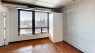 This contemporary 670 square foot apartment offers a harmonious blend of modern amenities and industrial charm. The open-concept layout maximizes space, featuring a combined kitchen and living area. The kitchen boasts honey-toned wooden cabinets, sleek black countertops, and stainless steel appliances, including a full-sized refrigerator and oven. A central island with bar seating provides additional prep space and casual dining options.

The living area flows seamlessly from the kitchen, characterized by warm hardwood flooring that extends throughout most of the apartment. Large windows allow ample natural light, while exposed concrete ceilings and visible ductwork add an urban, loft-like aesthetic.

The spacious 190 square foot bedroom offers a retreat with carpeted flooring for comfort. A built-in closet provides essential storage space. The bathroom features modern fixtures, including a vanity with storage and a shower/tub combination.

Additional highlights include in-unit laundry facilities and blinds for privacy. The apartment's industrial-chic design is softened by the warmth of the wood elements, creating a balanced and inviting living space perfect for urban dwellers seeking both style and functionality.