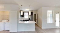 Located at 1421 Legacy Falls Dr in Wake Forest, NC, this single-floor residence showcases a clean, contemporary design with neutral tones and light wood-style flooring carried throughout the main living areas. The open-concept kitchen is a standout feature, equipped with dark espresso cabinetry, white quartz countertops, a curved peninsula with pendant lighting, and a full suite of stainless steel appliances including a refrigerator with ice maker, electric range, and built-in microwave. A dedicated pantry with built-in shelving adds practical storage. The living and dining areas flow naturally from the kitchen, benefiting from an open layout and ample natural light. Bedrooms are generously sized, with large windows framing views of the surrounding greenery, and ceiling fans for year-round comfort. One bedroom features light hardwood-style flooring, while another is finished with plush carpet. Closet space is well-appointed throughout. The bathroom presents a streamlined vanity with dark cabinetry, white countertop, and a window that brings in natural light. Clean lines and consistent finishes give the entire space a cohesive, modern aesthetic, making it a well-appointed home in Wake Forest.